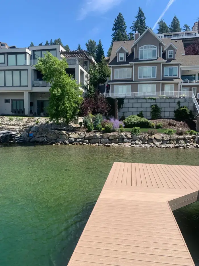 View from a dock looking back at lakefront properties featuring natural stone rock walls along the waterline, colourful planted beds, and a new composite dock in the foreground.