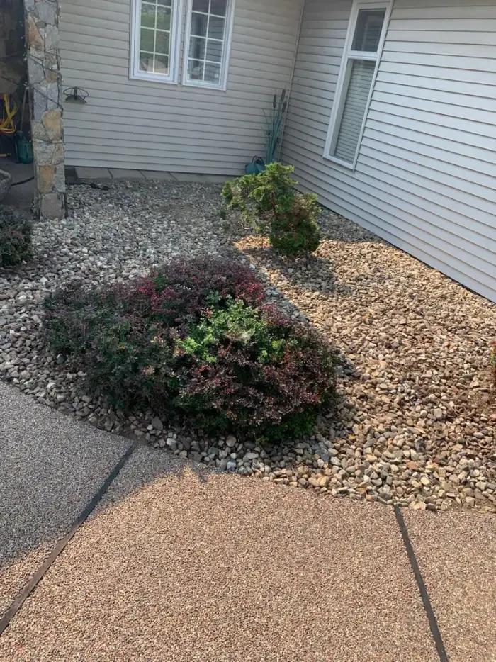 Round river rock ground cover installed around a covered pool area with trimmed shrubs and a rural Okanagan property with mountains in the background.