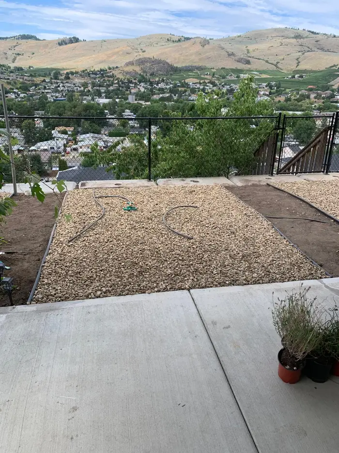 Crushed gravel ground cover freshly installed on a hillside terrace with drip irrigation in place and a sweeping Okanagan valley panorama stretching to the horizon.